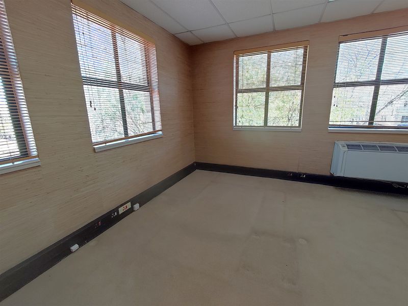 A vacant office space featuring neutral wall finishes, carpet flooring, suspended ceiling tiles, and integrated HVAC unit with natural light from multiple windows.