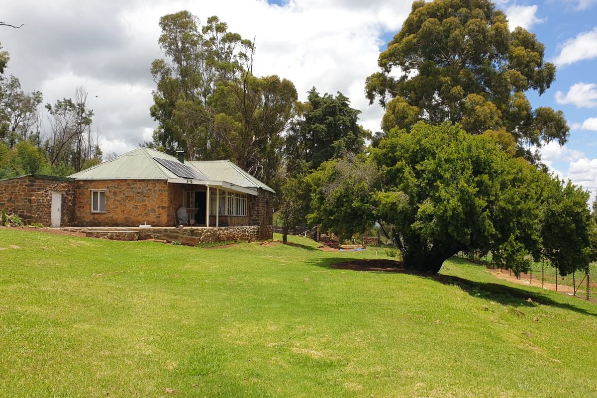 A charming stone-built farmhouse featuring a corrugated metal roof, solar panels, and a covered patio, set within a spacious, well-maintained garden landscape.