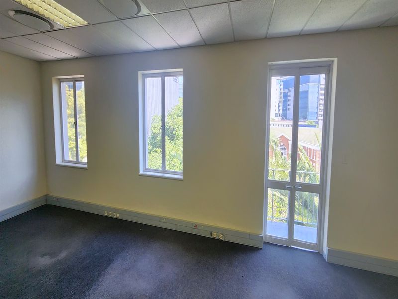 An empty office space featuring a suspended ceiling, recessed lighting, and multiple windows providing natural light and urban views.