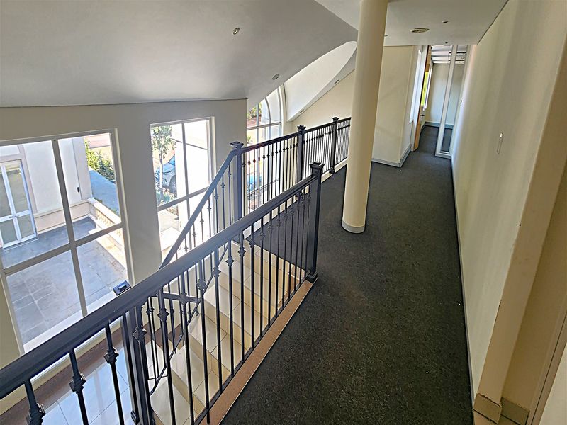 A spacious office hallway featuring a wrought iron balustrade overlooking the staircase, large windows for natural light, and a central structural column.