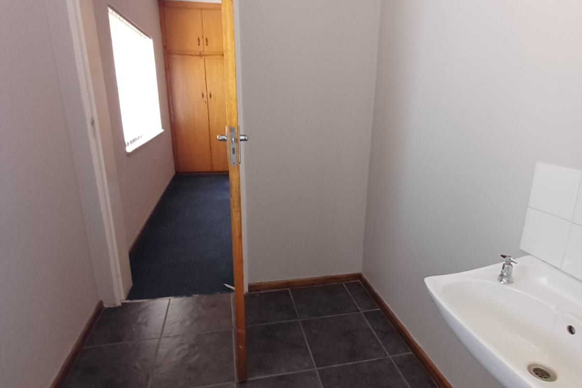A functional bathroom featuring a pedestal basin and toilet, with tiled flooring and a doorway leading to an adjacent room with built-in storage.
