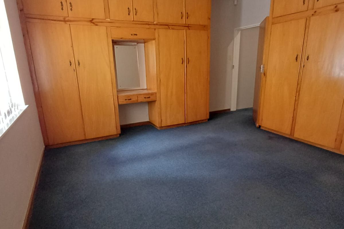 Spacious bedroom featuring extensive built-in wooden cabinetry with an integrated vanity unit and carpeted flooring.
