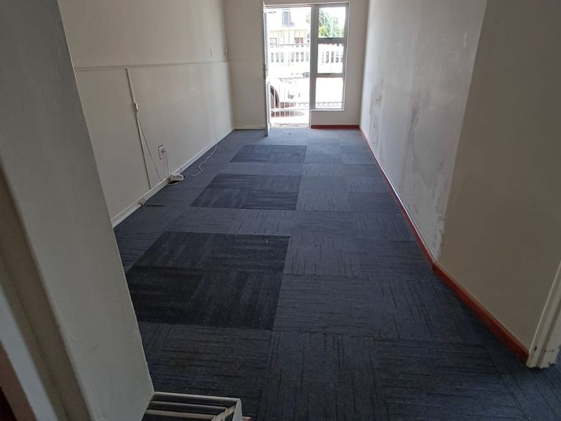 An empty office space featuring dark carpet tiles, a glass panel door, and visible wall surface wear requiring maintenance.
