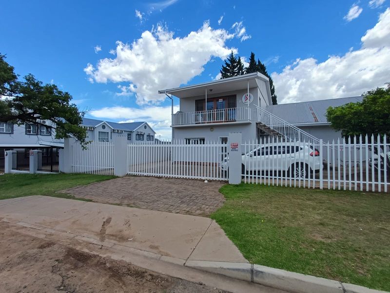 Front view of a two-story commercial property featuring a paved driveway, secure metal perimeter fencing, and an external staircase leading to an upper balcony.