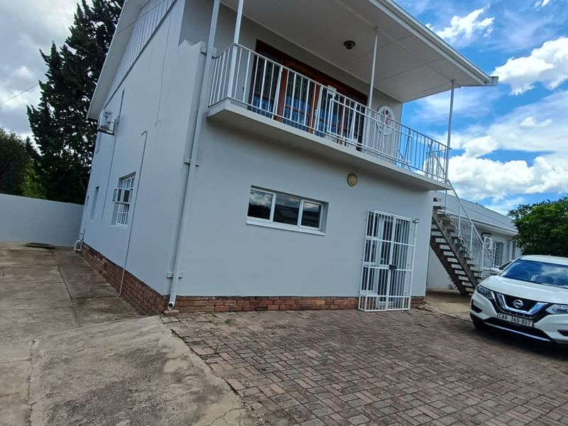 Rear view of a two-story building featuring a balcony, external metal staircase, security gate, and paved driveway area.