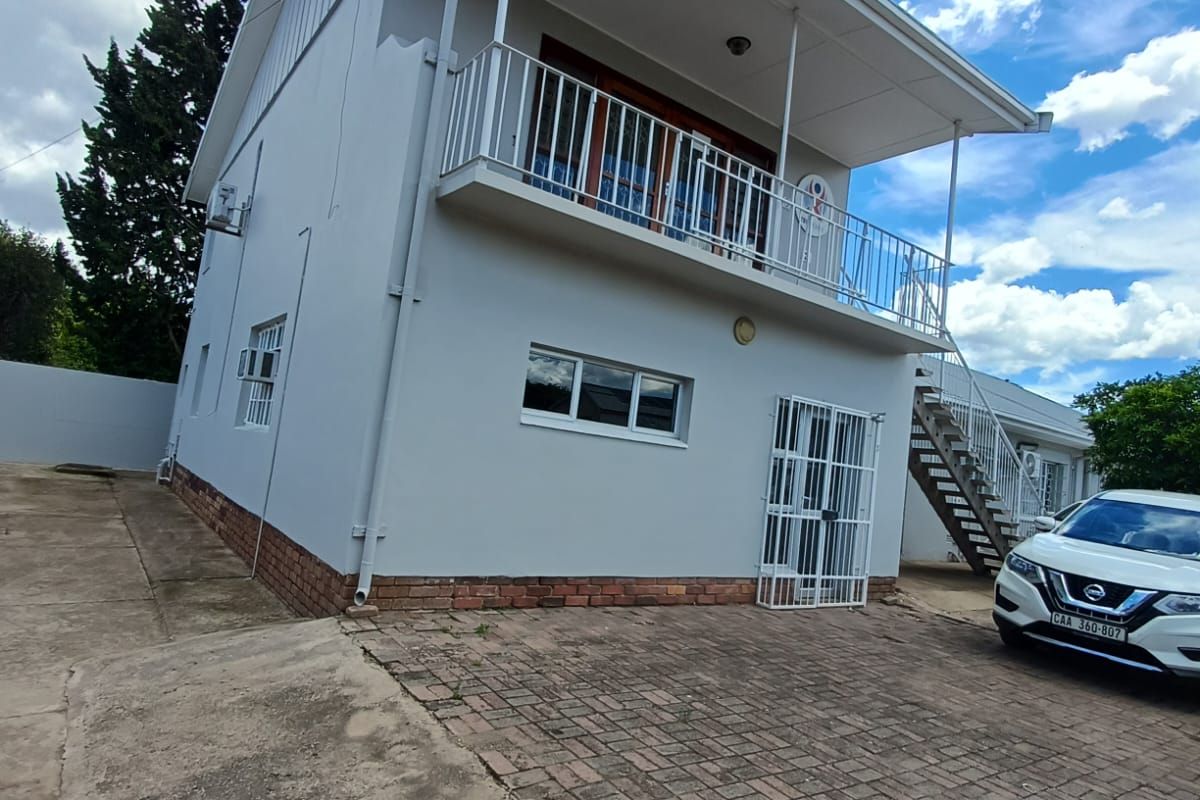 Rear view of a two-story building featuring a balcony, external metal staircase, security gate, and paved driveway area.