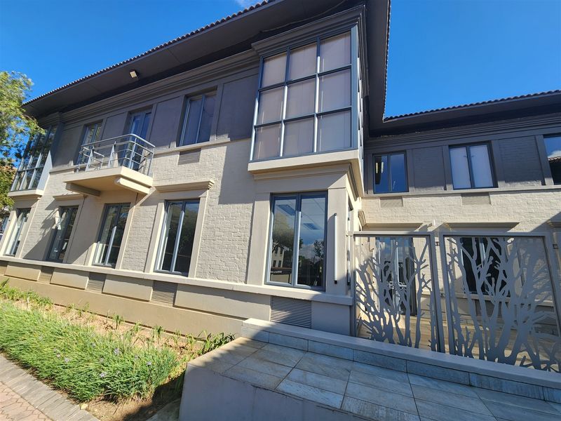 A modern office building exterior featuring a brick facade, large windows, a small balcony, and decorative metal entrance gates.
