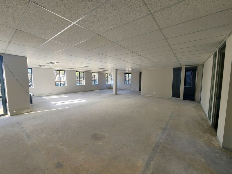A spacious, open-plan office area featuring a suspended ceiling, recessed lighting, and large windows, currently in a shell condition ready for fit-out.