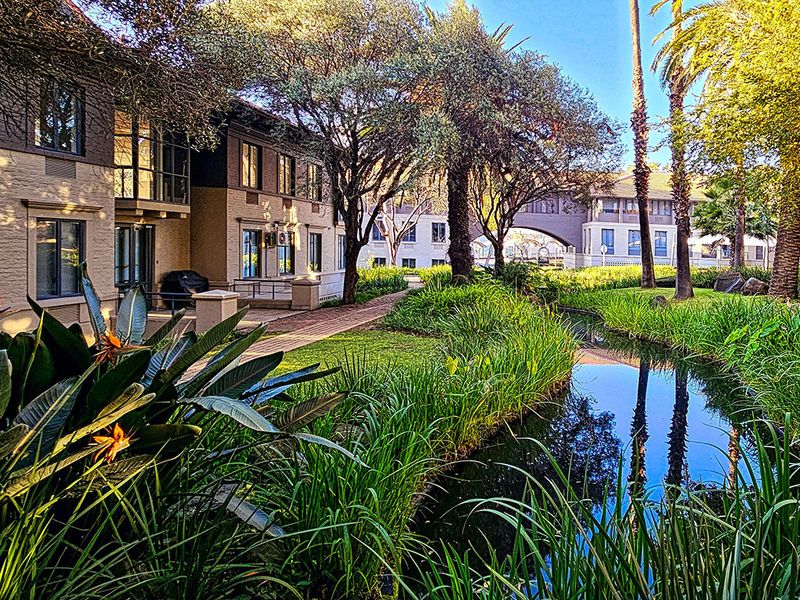A scenic view of the office complex exterior featuring a landscaped garden, a tranquil water feature, and paved walkways between building wings.