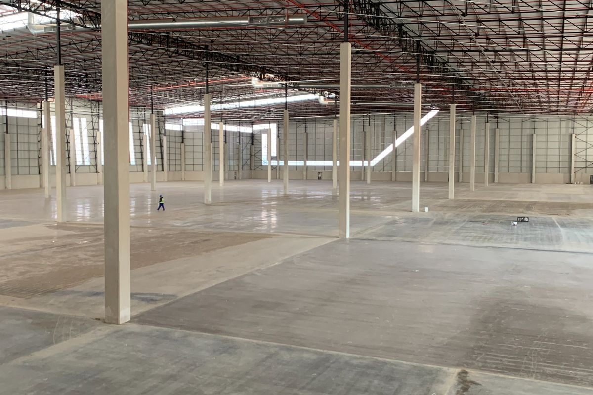 Expansive industrial warehouse space featuring high ceilings with exposed steel trusses, polished concrete flooring, and integrated fire sprinkler systems.