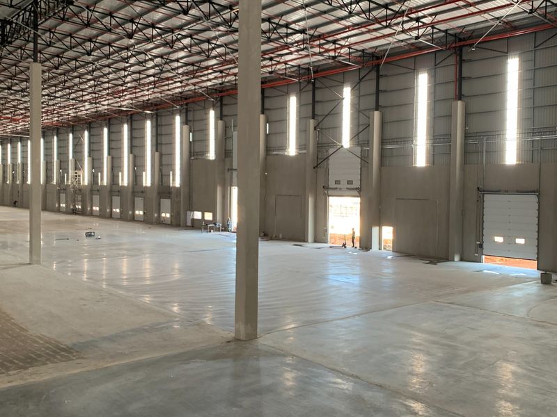 Spacious industrial warehouse featuring high ceilings, concrete flooring, multiple roller shutter doors, and robust steel truss construction, ideal for logistics or manufacturing operations.