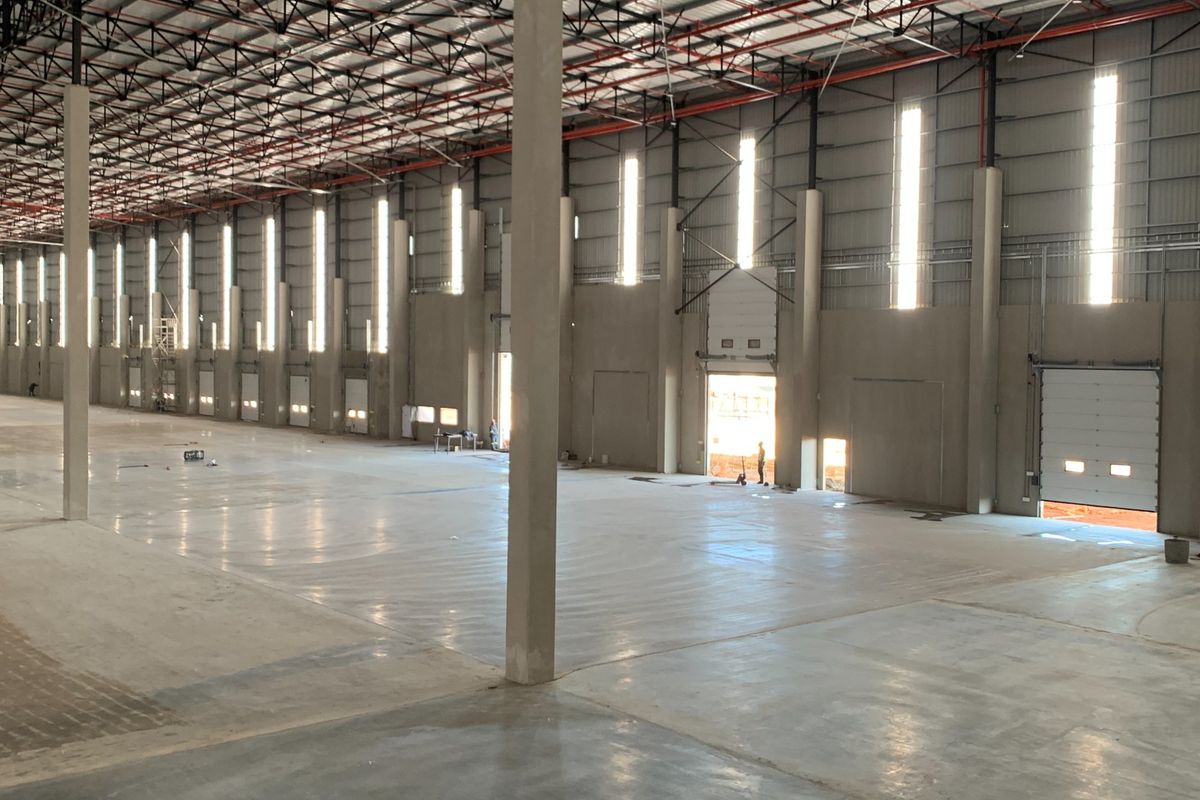 Spacious industrial warehouse featuring high ceilings, concrete flooring, multiple roller shutter doors, and robust steel truss construction, ideal for logistics or manufacturing operations.