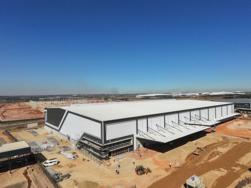 Aerial view of a large-scale industrial warehouse facility under construction, featuring a prominent cantilevered loading canopy and extensive site development.