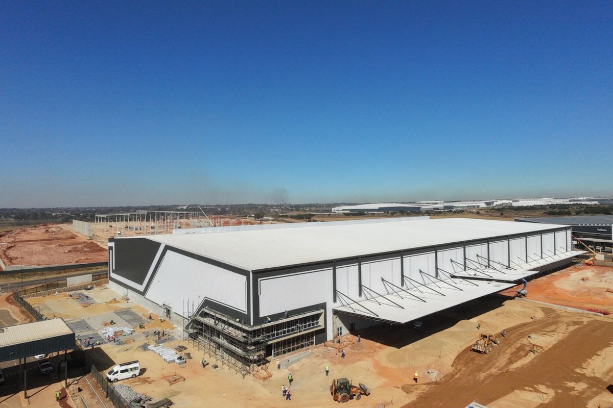 Aerial view of a large-scale industrial warehouse facility under construction, featuring a prominent cantilevered loading canopy and extensive site development.