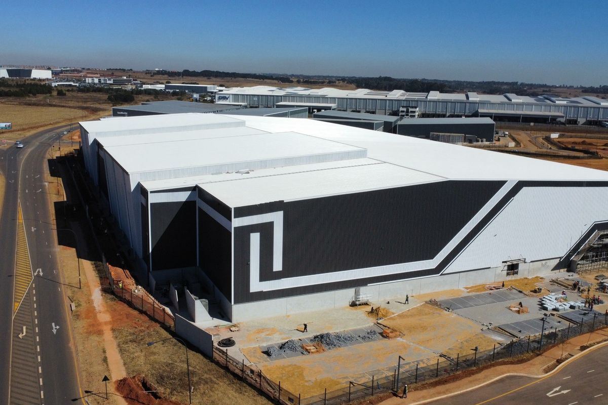 Aerial view of a large industrial warehouse facility featuring modern metal cladding, expansive roofing, and surrounding infrastructure in a developing industrial park.