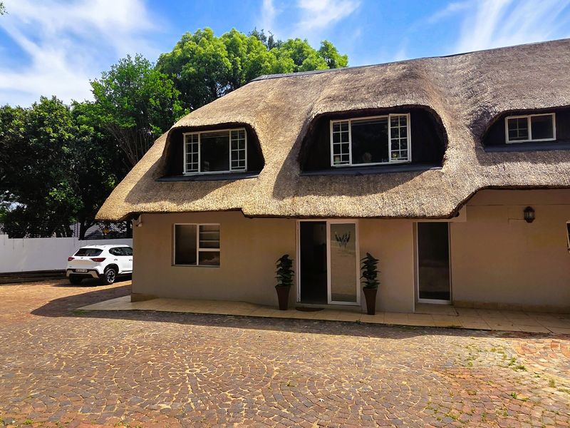 Front exterior view of a commercial property featuring a traditional thatched roof, paved driveway, and multiple casement windows.