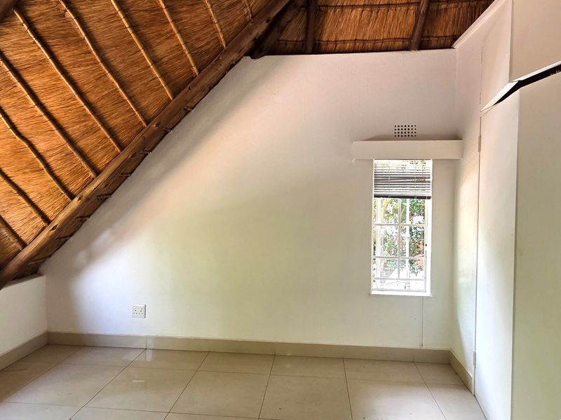 An empty bedroom featuring a unique vaulted thatched ceiling, tiled flooring, and a built-in cupboard, offering a bright and versatile living space.