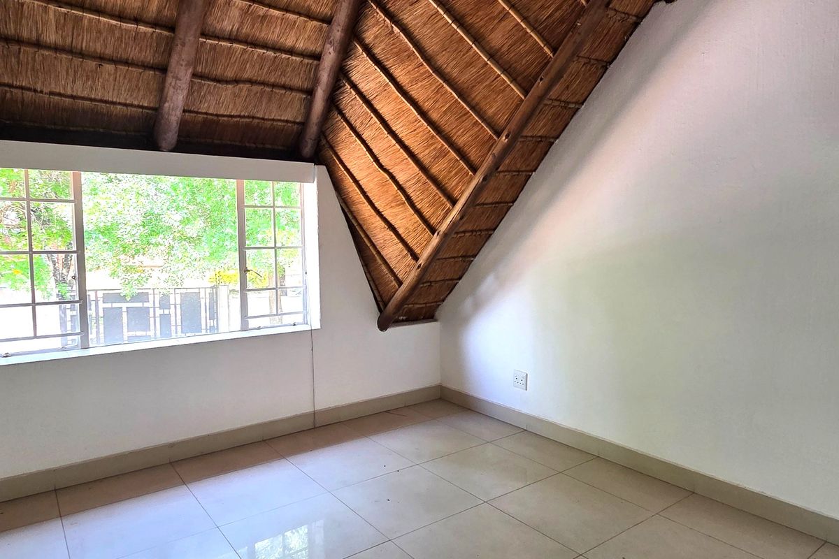 An empty bedroom featuring a unique thatched roof with exposed timber rafters, tiled flooring, and a large window providing natural light.