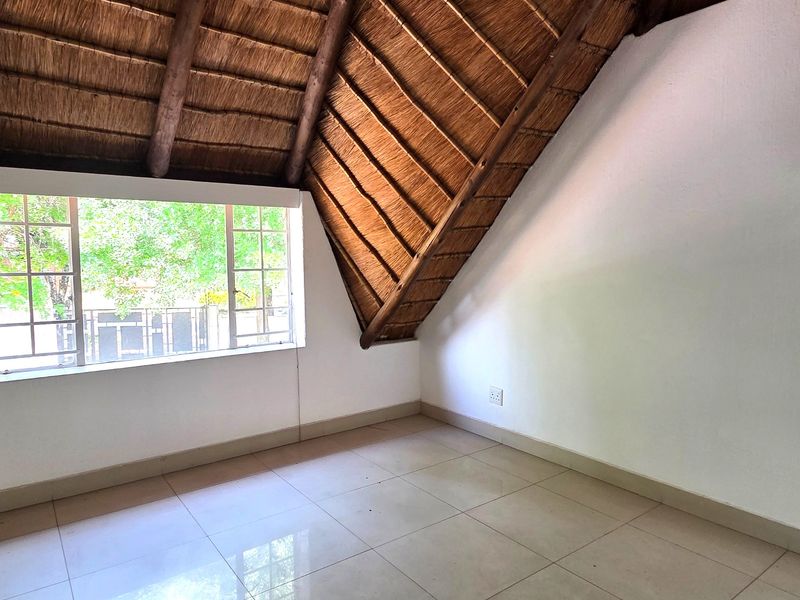 An empty bedroom featuring a unique thatched roof with exposed timber rafters, tiled flooring, and a large window providing natural light.