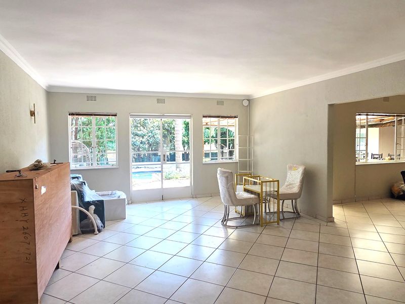 Spacious open-plan living area featuring neutral tiled flooring, large windows, and sliding glass doors providing direct access to the outdoor pool area.