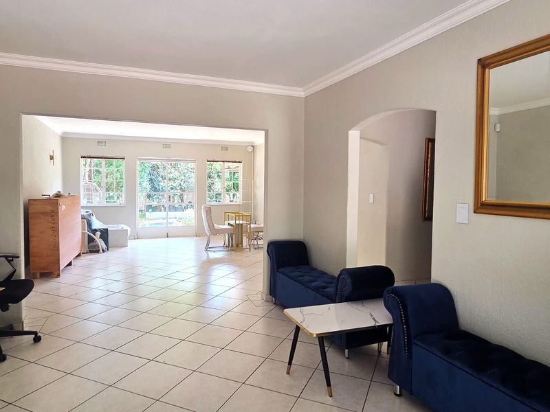 Spacious open-plan living area featuring neutral walls, crown molding, and ceramic tiled flooring, with an archway leading to an adjoining room and garden access.