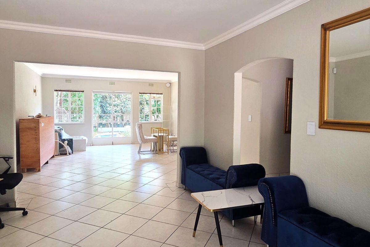 Spacious open-plan living area featuring neutral walls, crown molding, and ceramic tiled flooring, with an archway leading to an adjoining room and garden access.