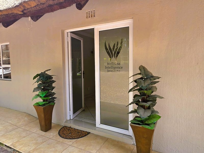 Entrance to the Wellness Intelligence Institute featuring a thatched roof overhang, tiled patio, and modern aluminium-framed glass door.