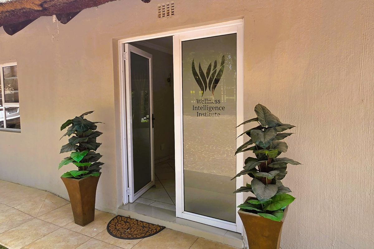 Entrance to the Wellness Intelligence Institute featuring a thatched roof overhang, tiled patio, and modern aluminium-framed glass door.