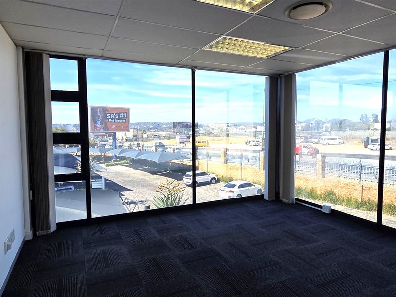 A bright, empty office space featuring expansive floor-to-ceiling windows, carpeted flooring, and a suspended ceiling with integrated lighting.