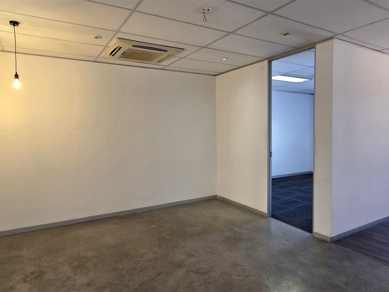 A bright, modern office space featuring a mix of concrete and laminate flooring, suspended ceilings, and integrated air conditioning.
