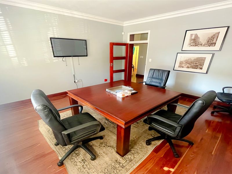 A well-maintained office space featuring polished hardwood flooring, crown molding, and a classic timber door with a transom window.
