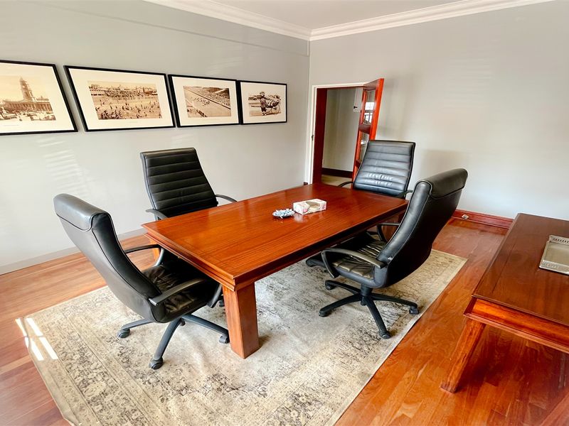 A professional office space featuring polished hardwood flooring, crown molding, and neutral wall finishes, suitable for a meeting room or executive workspace.