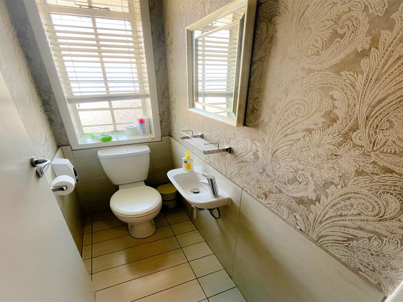A compact office bathroom featuring a toilet, wall-mounted basin, tiled flooring, and decorative wallpaper.