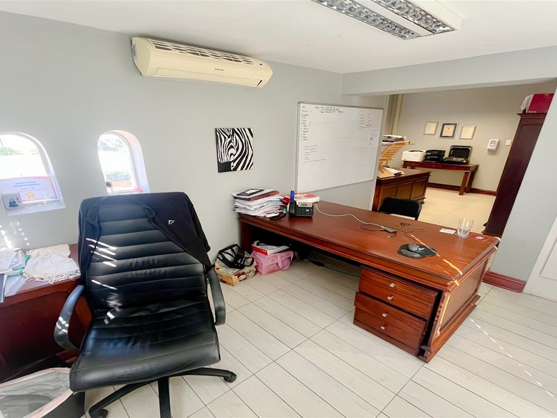 A functional office space featuring tiled flooring, arched windows, built-in whiteboard, and wall-mounted air conditioning unit.