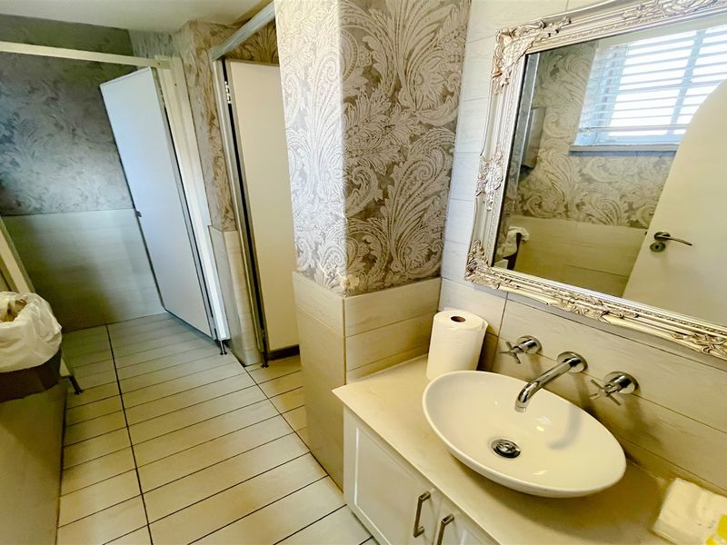 A functional bathroom featuring a vessel sink, wall-mounted faucet, vanity cabinet, and decorative wallpaper with tiled wall and floor finishes.