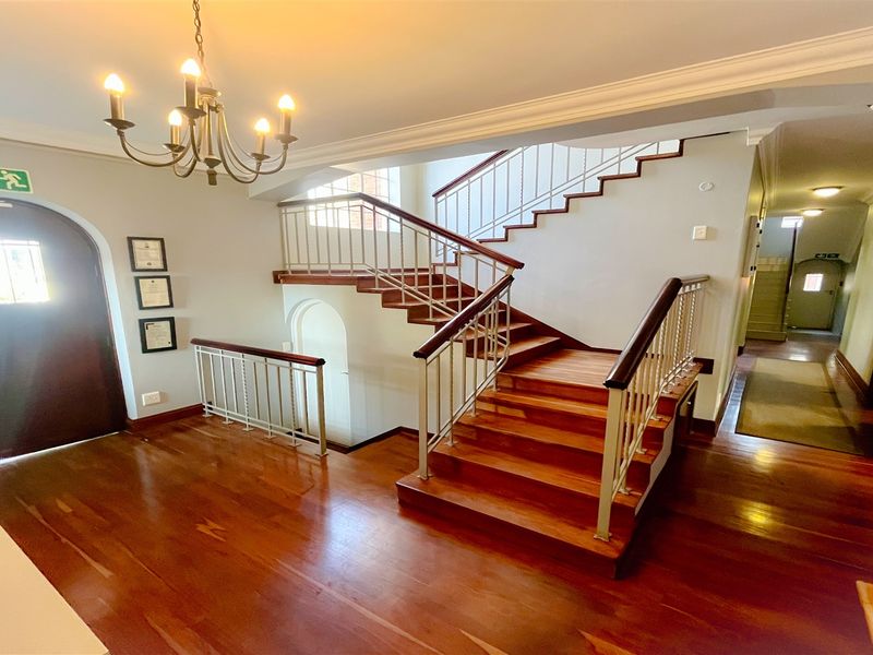 Spacious office entrance hall featuring a grand wooden staircase, polished hardwood flooring, and elegant architectural details including crown molding and an arched doorway.