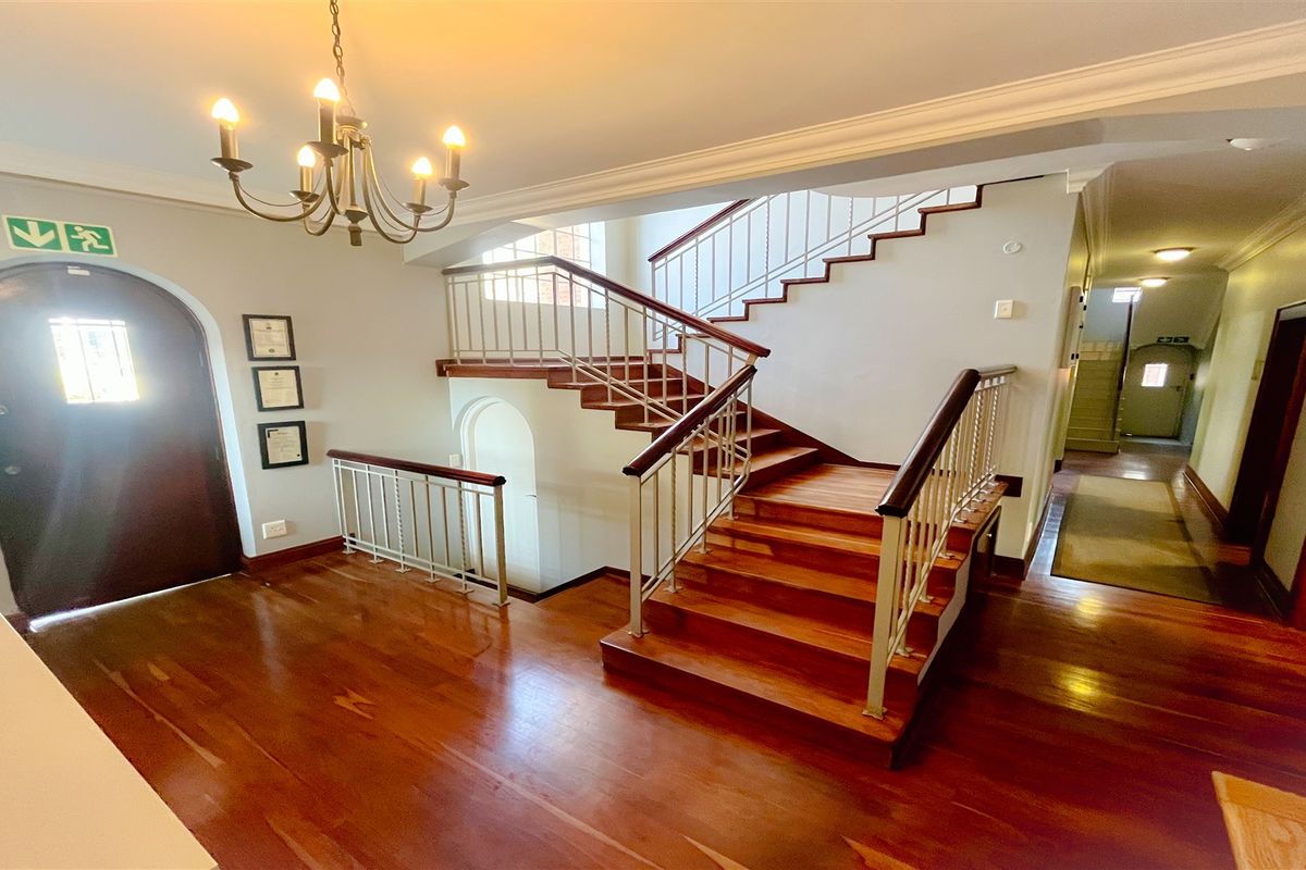 Spacious office entrance hall featuring a grand wooden staircase, polished hardwood flooring, and elegant architectural details including crown molding and an arched doorway.