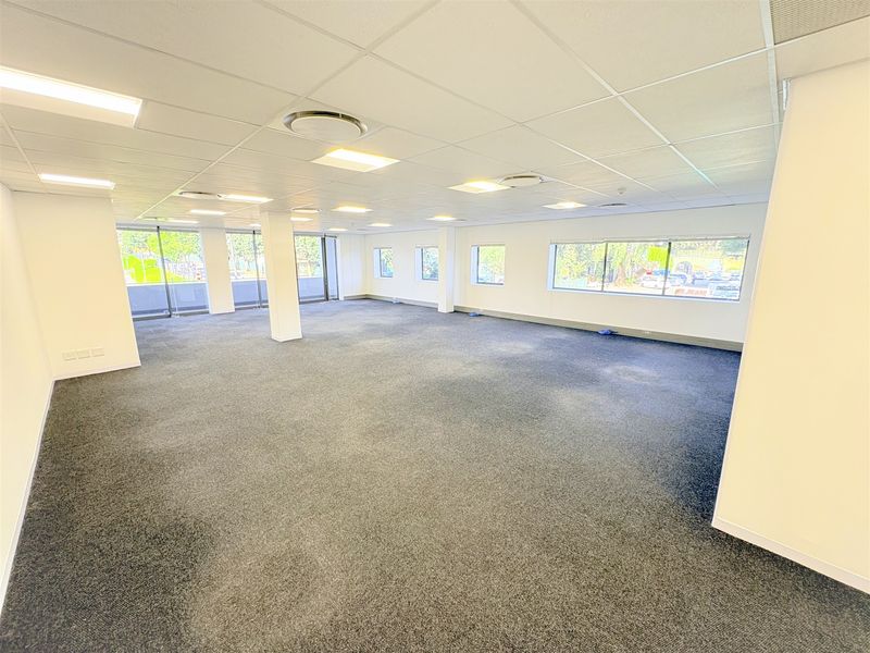 A spacious, open-plan office area featuring a suspended ceiling, recessed lighting, and large windows providing ample natural light.