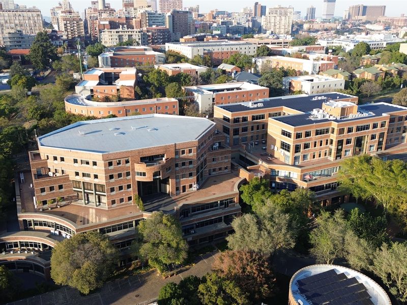 An aerial view of a large, multi-story brick office complex featuring flat roofs, integrated skylights, and rooftop solar panels within an urban setting.