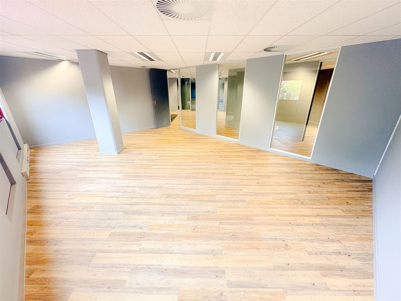 A spacious, modern open-plan office area featuring light wood-look laminate flooring, glass partitioning, and a clean, neutral aesthetic suitable for professional use.