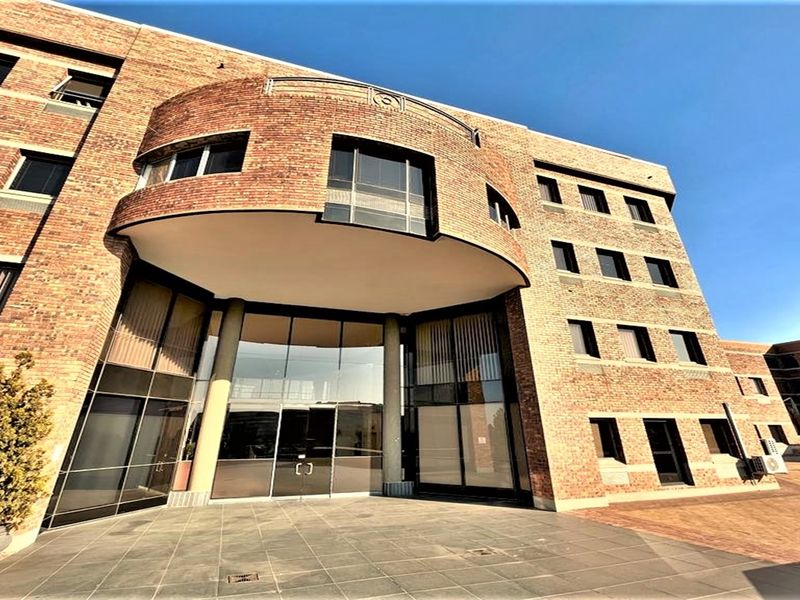 A professional multi-story office building featuring a distinctive curved brick facade, large glass entrance, and paved exterior approach.