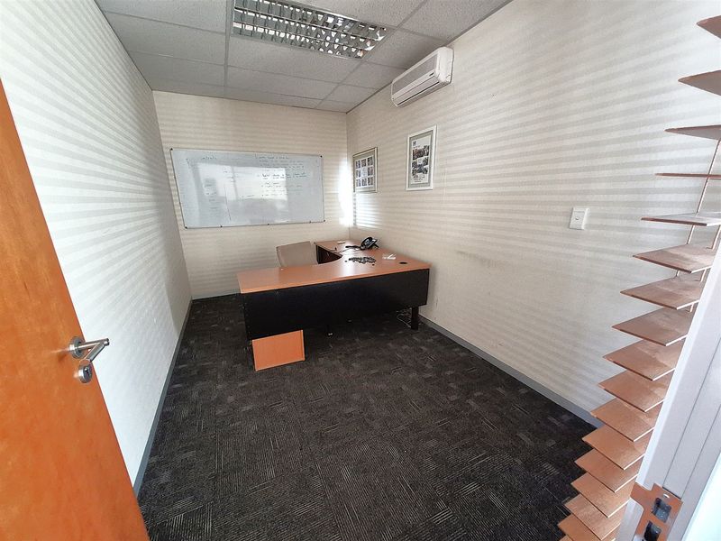A functional office space featuring carpeted flooring, a suspended ceiling with recessed lighting, and a wall-mounted air conditioning unit.