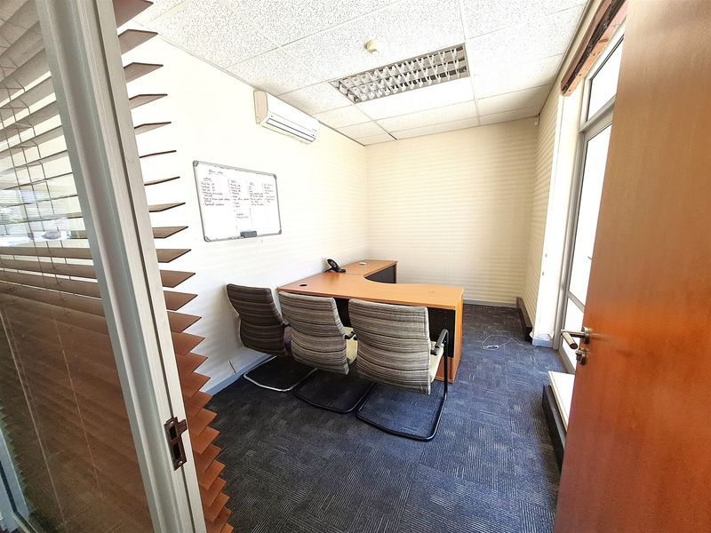A functional office space featuring carpeted flooring, a suspended ceiling with recessed lighting, and a wall-mounted air conditioning unit.