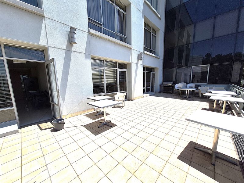 A spacious outdoor patio area featuring tiled flooring, large glass sliding doors, and modern glass facade elements, suitable for office break-out or social space.