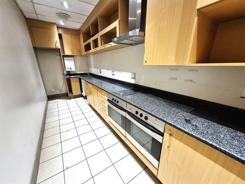 A functional office kitchen area featuring built-in wooden cabinetry, granite countertops, a double oven, and an electric hob with an extractor fan.
