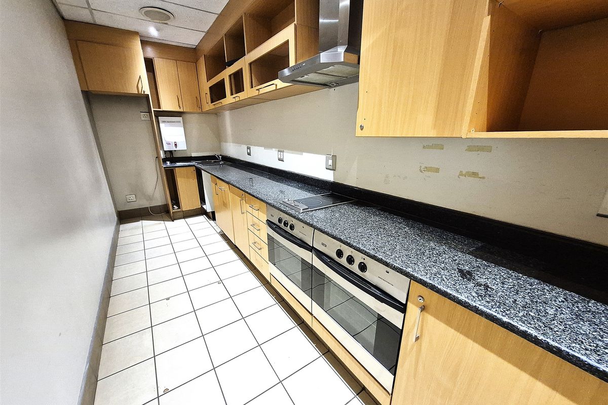 A functional office kitchen area featuring built-in wooden cabinetry, granite countertops, a double oven, and an electric hob with an extractor fan.