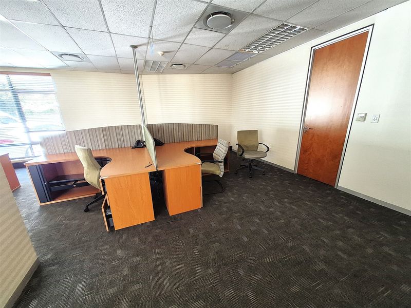A functional office space featuring a suspended ceiling, recessed lighting, carpeted flooring, and built-in workstation partitions, suitable for a professional work environment.