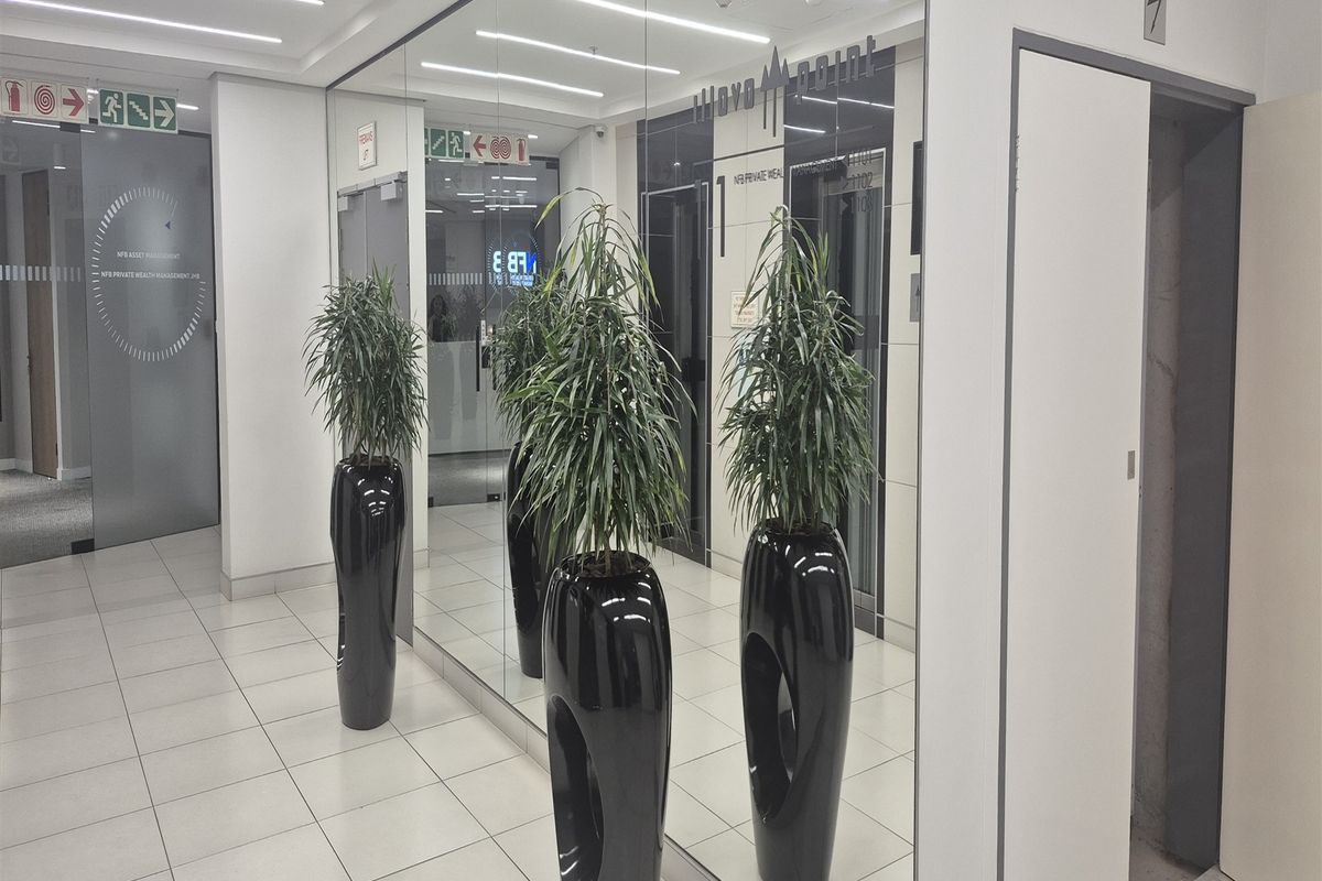 Modern office building hallway featuring tiled flooring, recessed linear ceiling lights, mirrored wall panels, and elevator access.