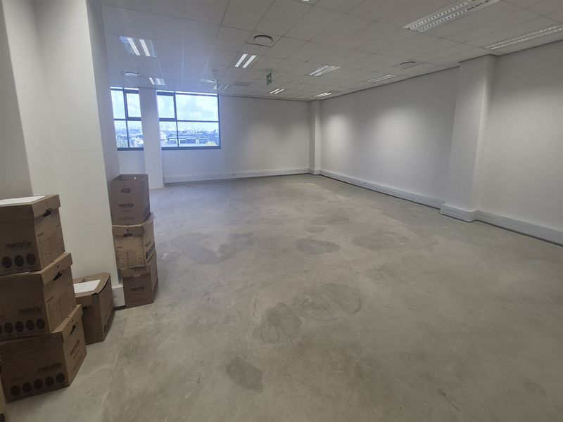 An empty, open-plan office space featuring a suspended ceiling, recessed lighting, and large windows providing natural light.