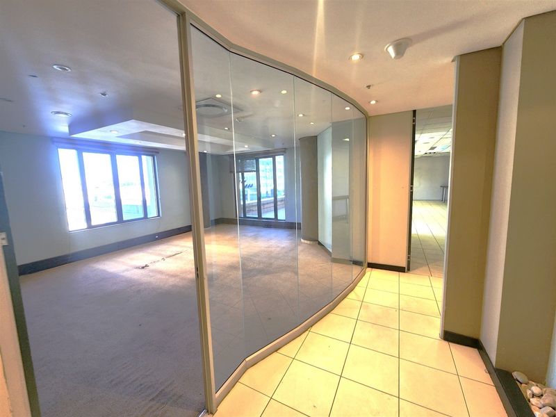 An empty office space featuring a curved glass partition wall, recessed lighting, and a combination of tiled and carpeted flooring.